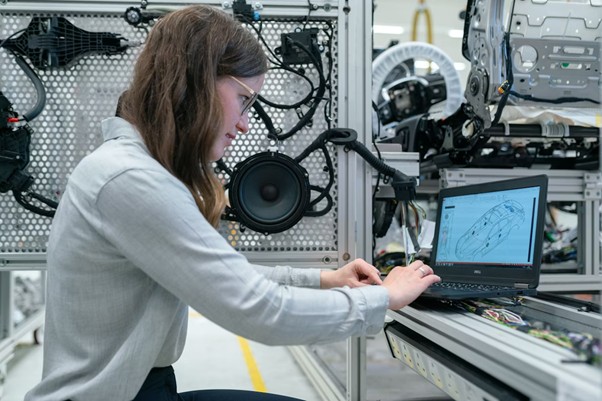 Image showing a woman surrounded by car parts while looking at a laptop.