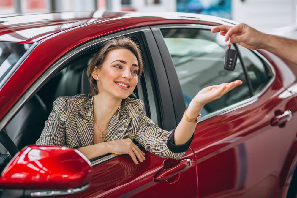 A woman smiling and receiving a car key and advice from a car seller while sitting in her new car, learning the best way to buy a car and making an informed decision.