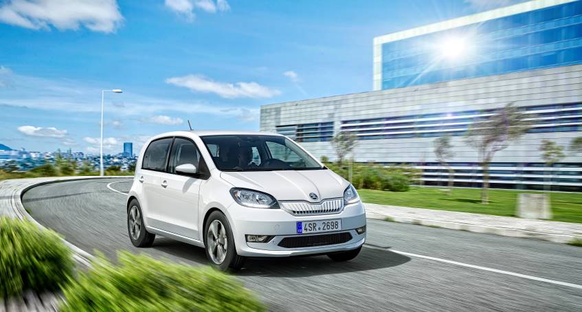 Small white 4 door Skoda Citigoe car driving on right hand side of a road in daytime