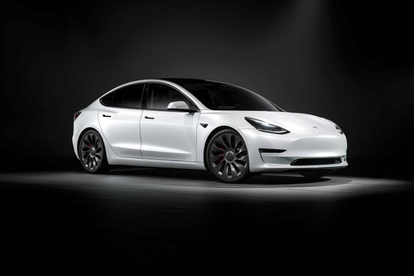 White 4 door Tesla Model 3 parked under a spotlight with everything else blacked out