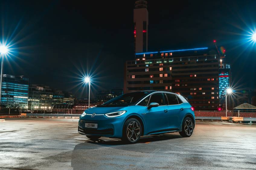 Bright blue 4 door VW car parked on the top floor of a car park at night with lights on